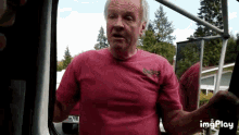 an older man in a pink shirt is standing in front of a mirror .