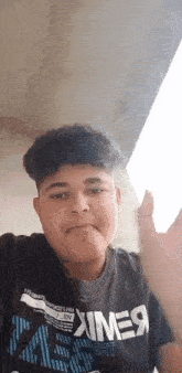 a young man with curly hair is wearing a black t-shirt and waving .
