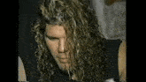 a man with long curly hair is wearing a black tank top .
