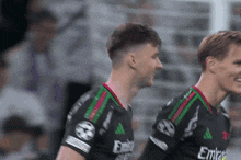 two soccer players wearing emirates jerseys are smiling