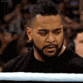 a man with a beard and a black shirt is standing in a boxing ring .