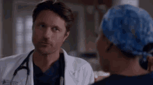 a man in a lab coat and stethoscope is talking to a woman in a scrub hat .