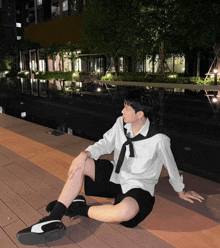 a man wearing a white shirt and black shorts sits on a wooden deck