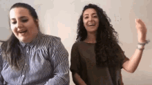 two women are standing next to each other and laughing . one of the women is wearing a striped shirt .