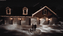 a couple standing in front of a house that has christmas lights on the roof