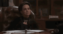 a woman sitting at a desk with her hand on her chest