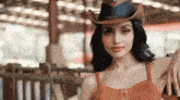a woman wearing a cowboy hat and an orange dress is posing for the camera .