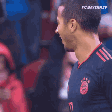 a man wearing a fc bayern jersey stands in front of a blurred crowd