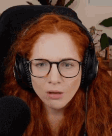 a woman with red hair and glasses is wearing headphones and making a funny face .