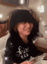 a woman wearing a seine paris hoodie is smiling while looking at her phone