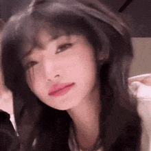 a close up of a woman 's face with a blurred background . she has long black hair and pink lips .