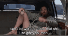 a man is sitting in the back seat of a car with his legs crossed and holding a glass of beer .