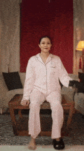 a woman in pink pajamas is sitting on a coffee table in a living room .