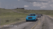 a blue rolls royce is driving down the road with other cars