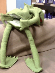 a stuffed green frog is laying on a couch holding a book