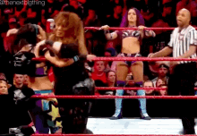 a couple of women wrestling in a ring with a referee in the background .