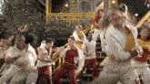 a group of people are dancing in front of a yellow building with a disney logo on the bottom right