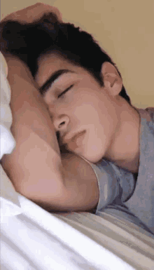 a young man sleeping on a bed with his hand on his head