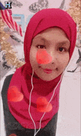 a woman wearing a pink hijab and ear buds with the letter h on the bottom right