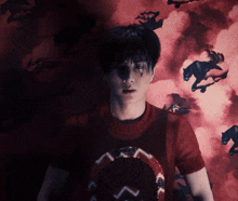 a man in a red shirt stands in front of a red background with horses on it
