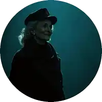 a woman wearing a hat and a black coat is smiling in a dark circle