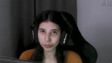 a young girl wearing headphones is sitting in a chair in front of a computer screen .