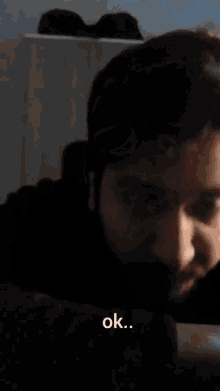 a man with a beard is looking at the camera and the word ok is above him