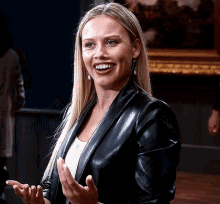 a blonde woman wearing a black leather jacket is smiling