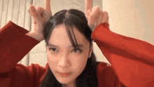 the girl is wearing a red sweater and making a funny face with her hands .