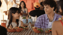 a boy and a girl are sitting at a table looking at each other and smiling