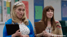 two women are standing next to each other in a classroom holding a clipboard .