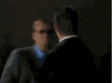 a man in a suit and sunglasses is talking to another man in a blue shirt .