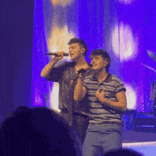 two men singing into microphones on a stage