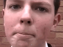 a close up of a young man 's face with a brick wall in the background making a funny face .