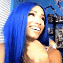 a woman with blue hair is smiling while standing in front of a window .