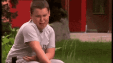 a young boy is sitting in the grass with his hands on his stomach and making a funny face .