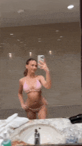 a woman in a pink bikini is taking a picture of herself in a bathroom mirror