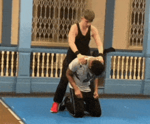 a man in a black tank top is wrestling another man in a white shirt