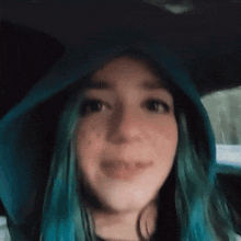 a woman with blue hair is wearing a blue hoodie and smiling .