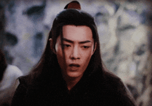 a close up of a man with long hair and a red knot in his hair