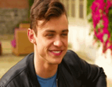 a young man wearing a leather jacket and a blue shirt is smiling while sitting on a porch .
