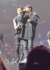 a man in a black hoodie is holding a microphone while standing next to another man in plaid pants