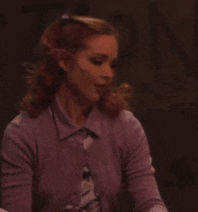 a woman wearing a purple cardigan and a floral shirt is standing in a dark room .