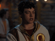 a young man with curly hair is wearing a white jacket with a red circle on it
