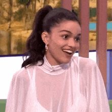 a woman in a white dress and ponytail is smiling and looking at the camera .