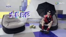 a man sitting on an inflatable chair holding an umbrella with a wetv logo on the wall behind him