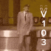 a man in a suit and tie is standing in front of a sign that says ' v1 0 3 '