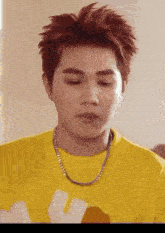 a young man with red hair is wearing a yellow t-shirt and a chain around his neck .