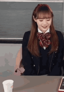 a girl in a school uniform is sitting at a table with a cup of coffee and a phone .