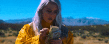 a woman in a yellow raincoat is holding a stack of 100 dollar bills .